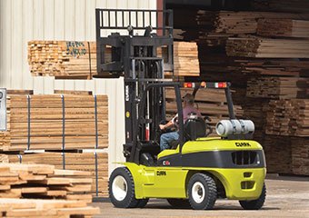 Worker hauling lumber with a Clark pneumatic LPG forklift