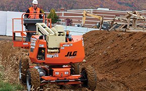 Worker driving a rough terrain boom lift through the mud